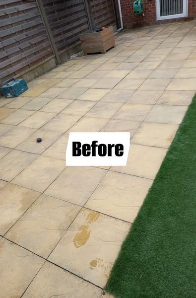 Paved patio with beige tiles and a patch of green artificial grass. A wooden planter is in the corner, and the word "Before" is centered on the image.