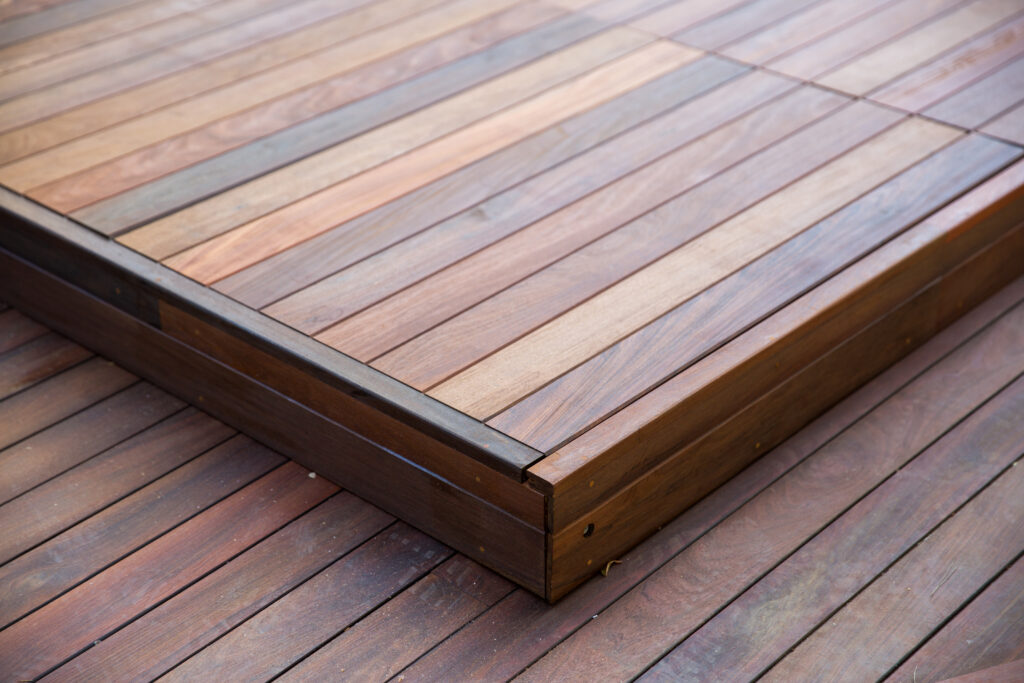 Close-up of a raised wooden deck platform with neatly aligned planks in varying shades of brown, contrasting with the darker wood flooring below.
